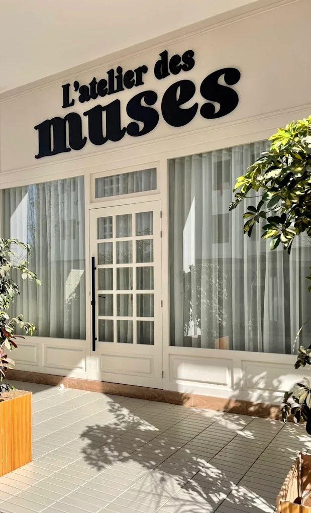 Devanture de L’atelier des muses, enseigne noire au-dessus de larges vitrines voilées